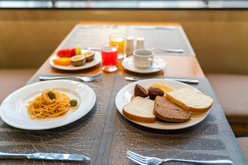 Fresh romantic breakfast table next to morning briliant light window, with bread, pastry, spaghetti, fruit, juice