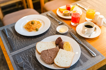 Fresh romantic breakfast table next to morning briliant light window, with bread, pastry, spaghetti, fruit, juice, coffee cup