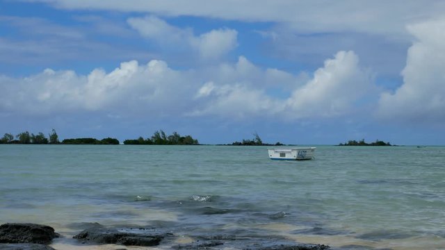 A idyllic scene of a small boat in a light blue sea, under a sky with beautiful clouds in a tropical island