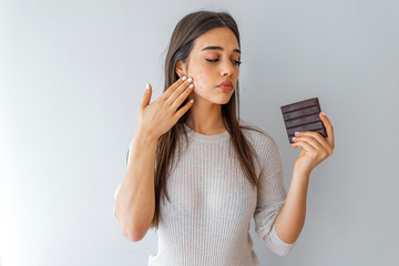 Young woman with acne problem holding chocolate bar on grey background. Skin allergy. Closeup Acne...