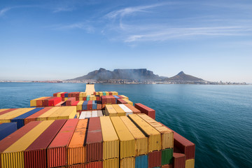 Groot gestapeld containerschip dat de haven van Kaapstad verlaat met de Tafelberg en de stad op de achtergrond, Zuid-Afrika.