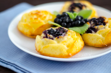 On the dish are three cheesecakes with blueberries and one without toppings, garnished with fresh blueberries and mint leaves. Composition on a textile napkin.