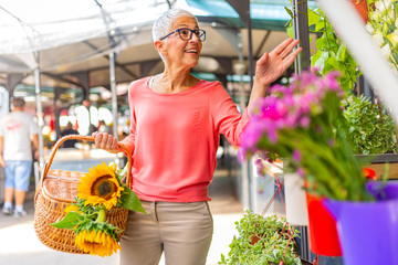 Portrait of a beautiful senior woman doing shopping in a market on a sunny morning, she carries a...
