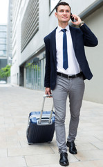 Man in suit with suitcase is talking by phone