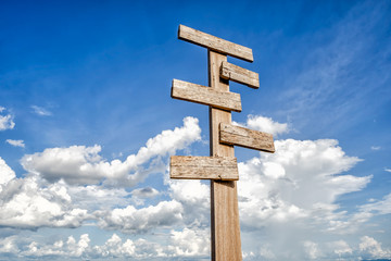 Old wooden signpost against blue sky with five sign choices pointing in different directions.