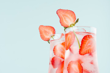 Cold summer strawberry water with strawberry slices, ice cubes, soda in misted glass on pastel green color background, closeup, half, edge, top.