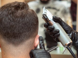 Hair cutting with clipper, males nape, close up view. Stylists hands in black rubber gloves with...