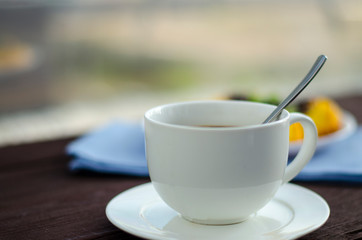On the dish are three cheesecakes with blueberries and one without toppings, garnished with fresh blueberries and mint leaves. Composition on a textile napkin with a cup of coffee.