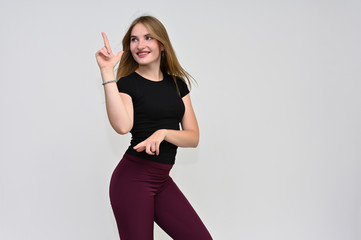 A knee-length portrait of a pretty brunette girl with long flowing hair in a black T-shirt and burgundy trousers on a white background. Smiling, showing emotions.