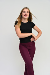 Naklejka premium Full-length vertical portrait of a pretty brunette girl with long flowing hair in a black t-shirt and burgundy trousers on a white background. Smiling, showing emotions.