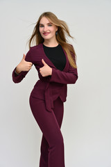 Fototapeta premium Full length vertical portrait of a pretty secretary manager brunette girl with long flowing hair in a burgundy business suit on a white background. Smiling, showing emotions.