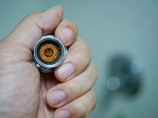 Close up of a hand holding a removed / disassembled part of a rain shower head getting clogged with mineral deposits, hardened lime and particulate matters, disrupting the water flow