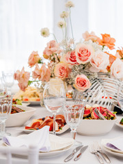 Table served for wedding banquet with cutlery and flowers in vases. Pastel colored decorations.