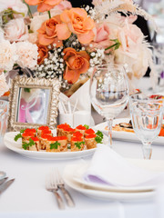 Table served for wedding banquet with cutlery and flowers in vases. Pastel colored decorations.