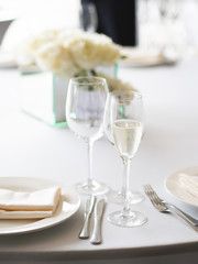 Table served for banquet with cutlery, wine glasses and napkins. Pastel colored decorations.