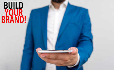 Word writing text Build Your Brand. Business photo showcasing creates or improves customers knowledge and opinions of product Business concept with man holding mobile phone with touch screen