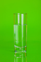 Glass cup of mineral water on green background