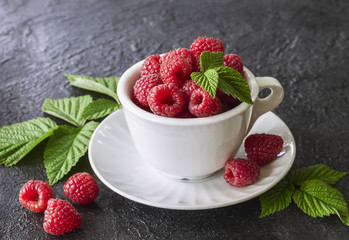 fresh raspberries in a white cup close-up. background with raspberry and green leaves.