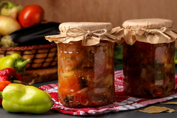 Vegetable salad with peppers, eggplant, onions and tomatoes in jars on a wooden table, horizontal...