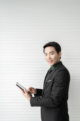 The happy businessman is holding the tablet and pointing his finger on the screen in a white background room. Business and technology concept.