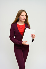 Vertical portrait of a pretty secretary manager brunette girl with long flying hair in a burgundy business suit with a folder in her hands on a white background. Smiling, showing emotions.