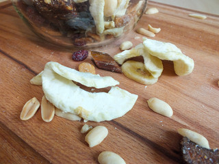 Dehydrated fruit of apple, banana, raisins, rhubarb and nuts from a glass jar on a wooden board.