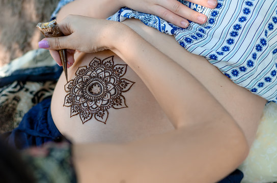 Master is drawing henna tatto on pregnant belly, closeup.  A mehendi artist paints a beautiful mandala. Motherhood concept, happy maternity