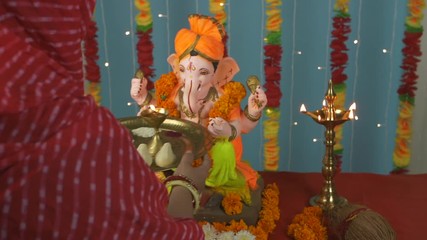 Overhead shot of an Indian female worshipping Lord Ganesha on Ganesh Chaturthi . A young female is praying in front of Ganesh Ji with thali in her hand - Decorated festival background in the temple...