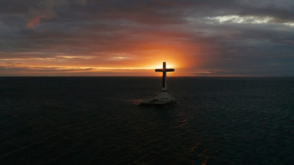 Catholic cross in sunken cemetery in the sea at sunset, aerial drone. colorful sky during the sunset. Large crucafix marking the underwater sunken cemetary, Camiguin Island Philippines.