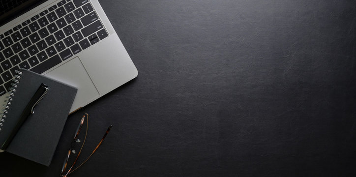 Top view of dark trendy workplace with laptop computer and office supplies on black leather desk