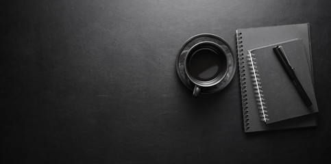 Dark modern workplace with coffee cup and notebook on black leather table background