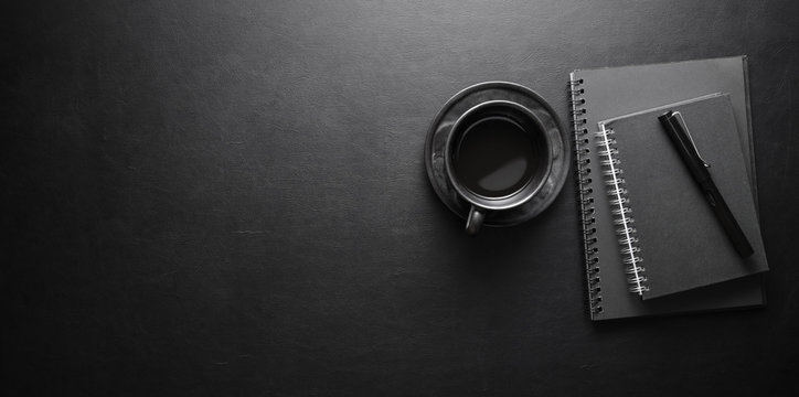 Dark modern workplace with coffee cup and notebook on black leather table background