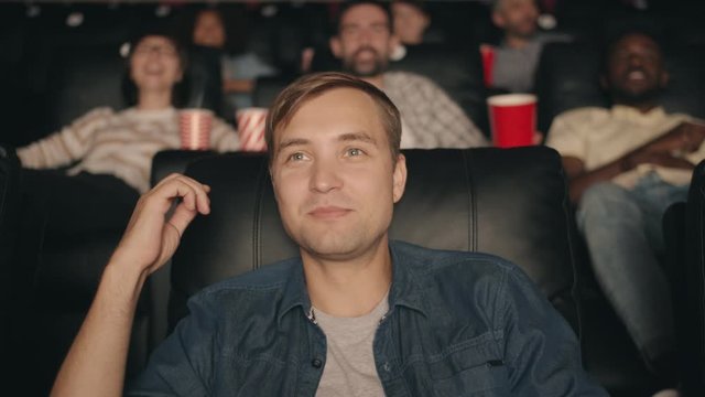 Slow motion of joyful young man watching movie in cinema with popcorn and fruit juice laughing having fun pointing at screen. Happiness and entertainment concept.