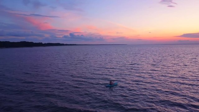 A dramatic drone shot of a lone kayaker slowly driffting into a colorful sunset