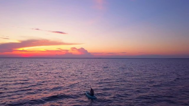 A dramatic drone shot of a lone kayaker slowly driffting into a colorful sunset