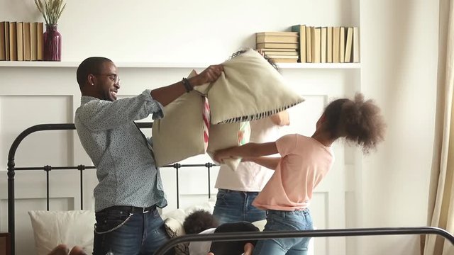 Overjoyed african family with kids play pillow fight on bed