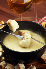 Gourmet Swiss fondue dinner on a winter evening with assorted cheeses on a board alongside a heated pot of cheese fondue with two forks dipping