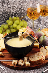 Gourmet Swiss fondue dinner on a winter evening with assorted cheeses on a board alongside a heated pot of cheese fondue with two forks dipping