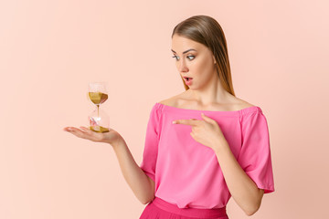 Shocked young woman with hourglass on color background