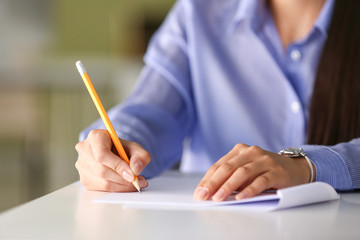 Young female student writing on sheet of paper, closeup