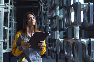 A young pretty white woman works in the paint shop of the plant, she checks the unpainted metall products and making record in check list.