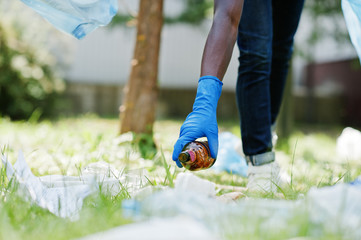 Hand of african american man picking up bottle into garbage bags while cleaning area in park....