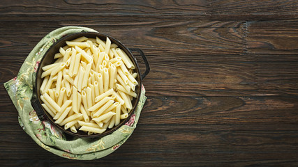 Ready-to-eat penne pasta in a pan on a wooden table. Vegetarian food. Overhead view
