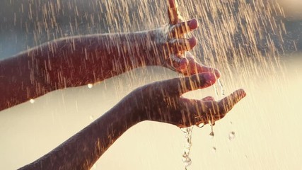 Water streams in the solar rays fall on the young woman's hands.