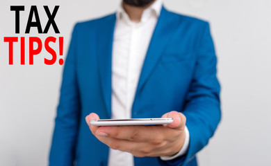 Word writing text Tax Tips. Business photo showcasing compulsory contribution to state revenue levied by government Business concept with man holding mobile phone with touch screen