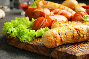 Tasty grilled sausages on wooden board, closeup