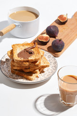 Appetizing toasts with chocolate paste, coffee with milk, figs and blueberries on the table.