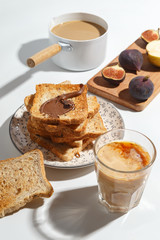 Appetizing toasts with chocolate paste, coffee with milk, figs and blueberries on the table.