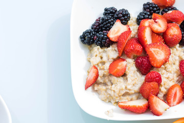 Close-up white bowl dish with oatmeal porridge with strawberries and blackberries. View from above. The concept of healthy vegetarian food and delicious breakfasts. DIY harvest. Copy space