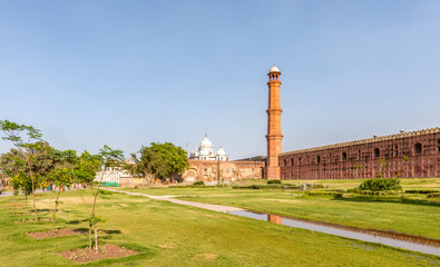 Wall and tower of the Badshahi Mosque or Imperial Mosque left and the Samadhi of Ranjit Singh white edifice, a Sikh shrine in Lahore, Punjab, Pakistan.